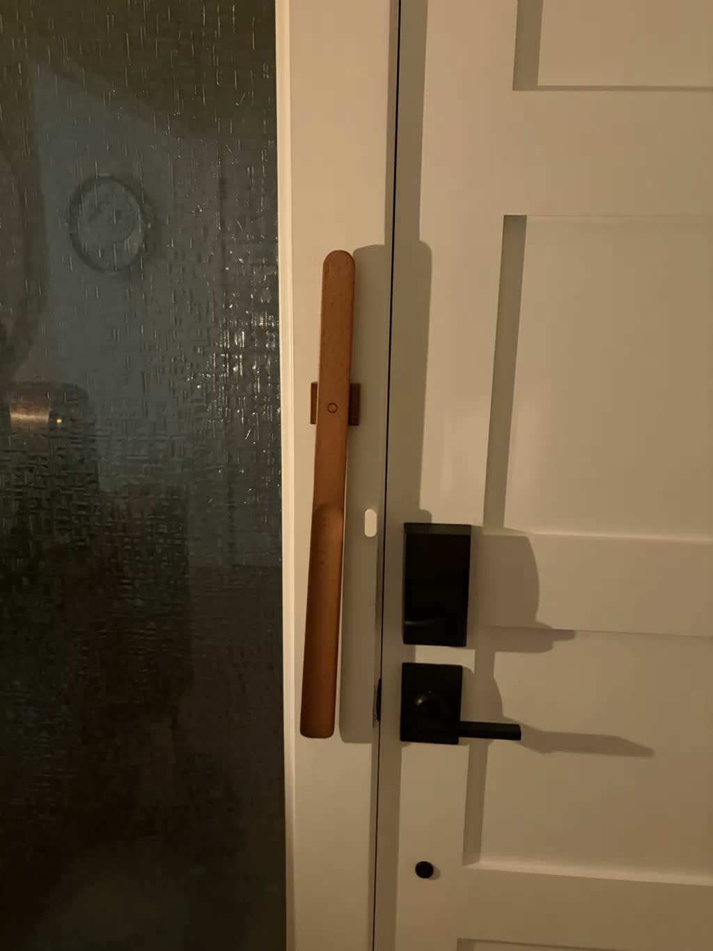 Vaalea pyökkinen kenkälusikka magneettikiinnityksellä valkoisessa ovenkarmissa mustan ovenkahvan ja älylukon vieressä